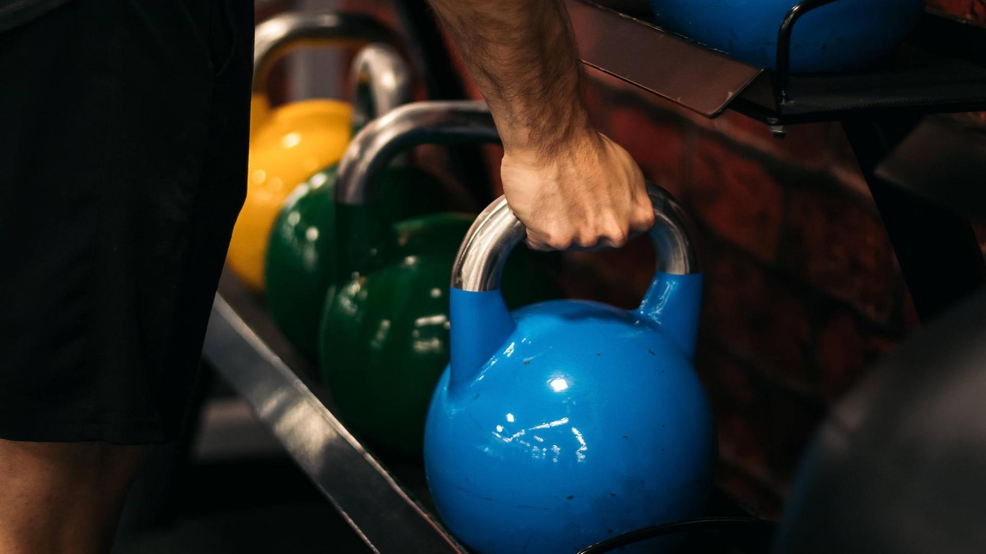 Ein Mann im Fitnessstudio greift ein Gewicht.