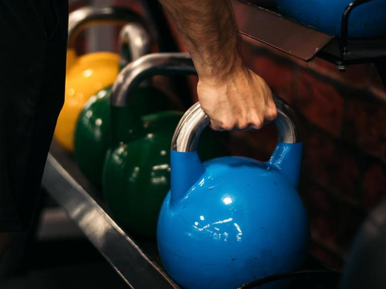 Ein Mann im Fitnessstudio greift ein Gewicht.