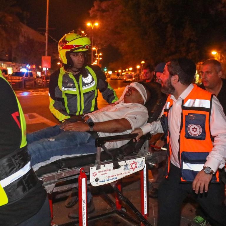 Rettungseinsatz nach Raketenbeschuss in Holon, Israel: Sanitäter tragen einen Mann auf einer Trage weg.
