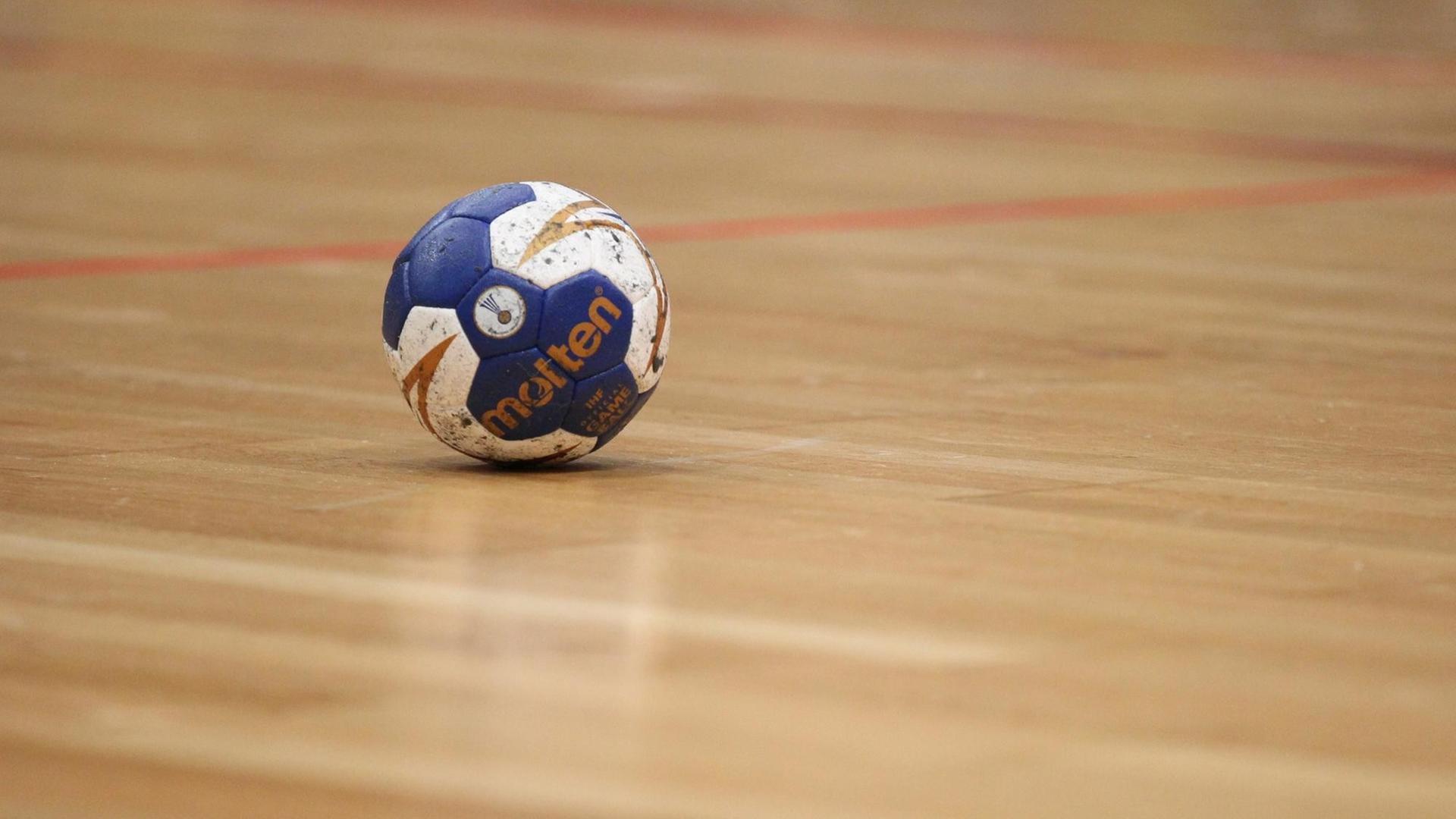 Ein Handball liegt auf den Hallenboden.