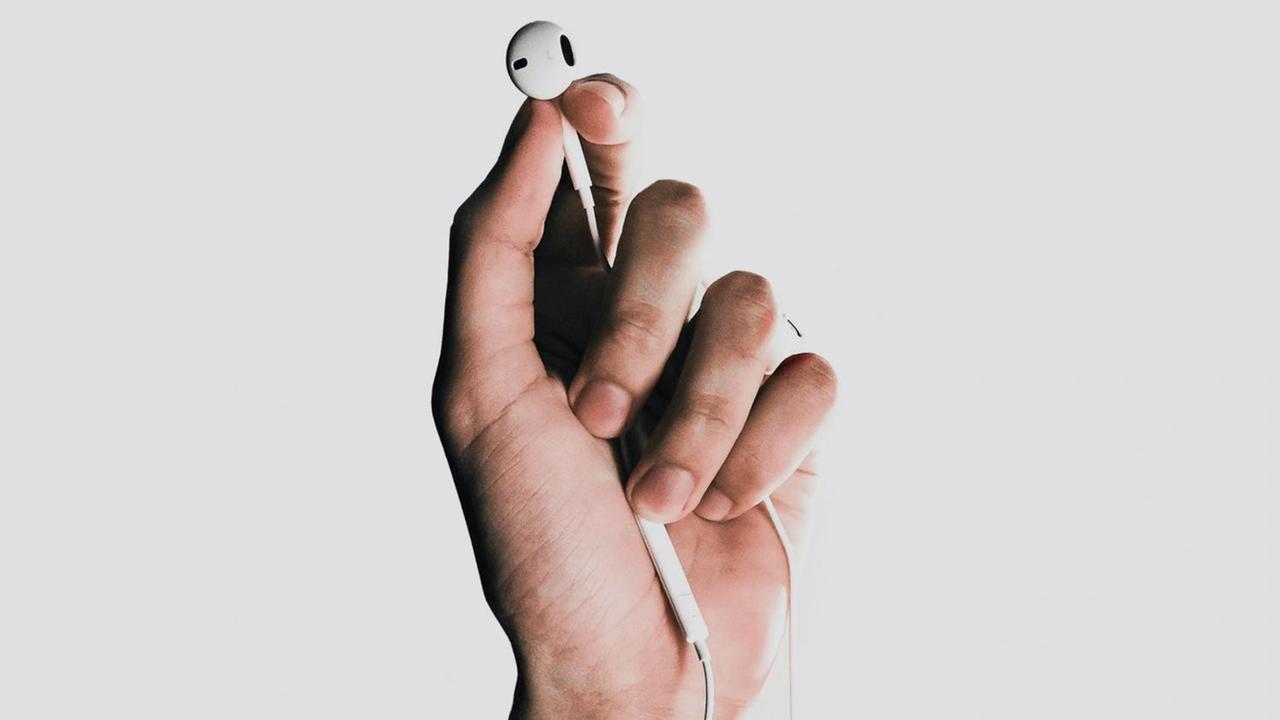Fotografie einer Hand, die einen weißen In-Ear-Kopfhörer  zwischen Daumen und Zeigenfinder hält.