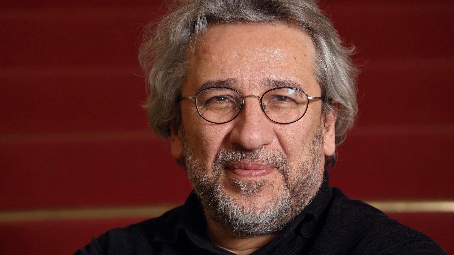 Can Dündar blickt lächelnd in Richtung des Betrachters.