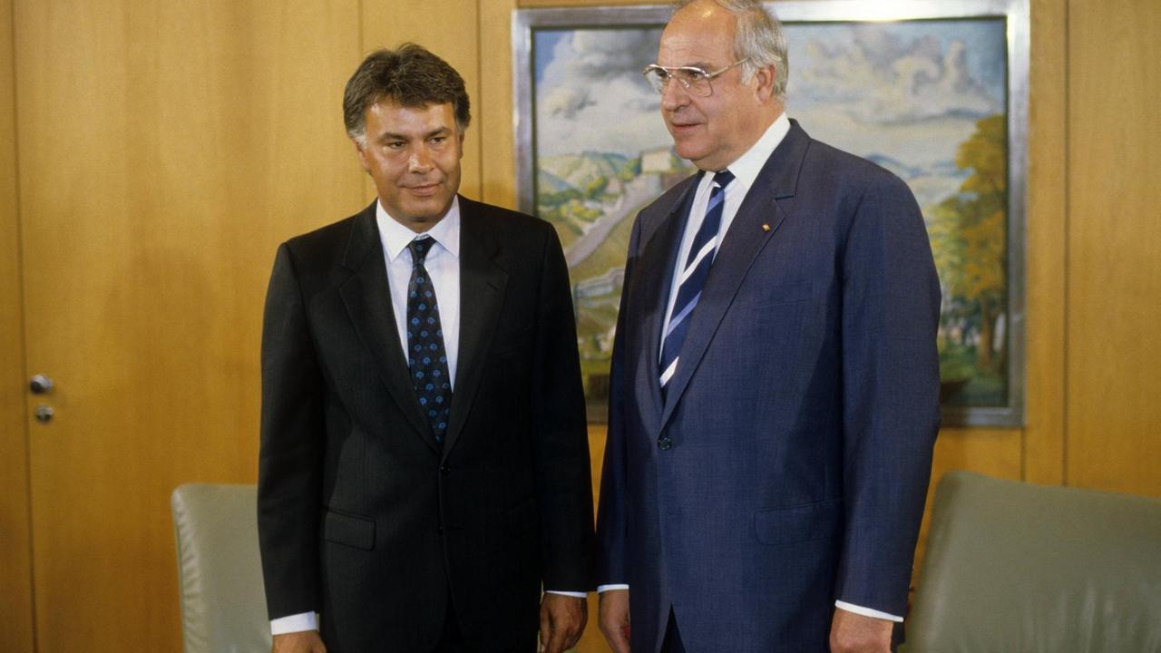 Felipe González und Helmut Kohl stehen vor einer Holzwand und lächeln.