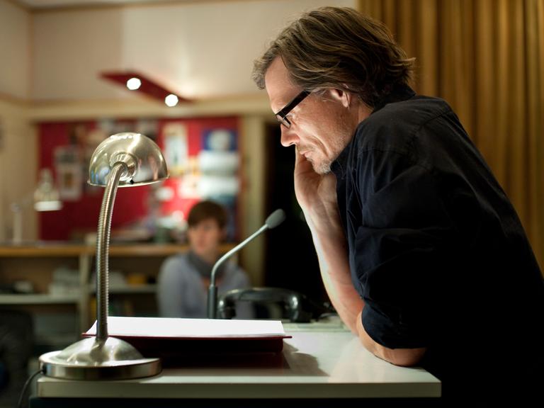 Der Regisseur Alexander Schuhmacher sitzt bei einer Studioaufnahme am Tisch.  