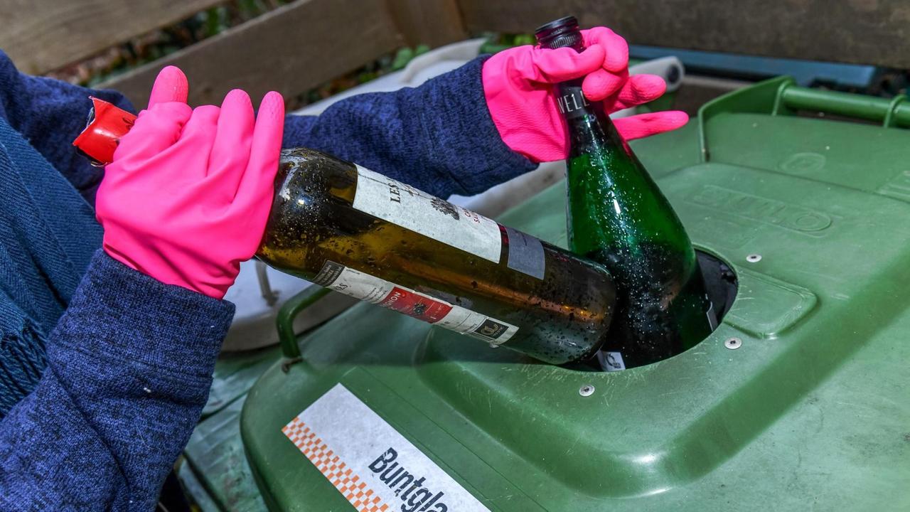 Eine Person mit pinken Gummihandschuhen wirft Flaschen in eine Altglastonne für Buntglas, aufgenommen 2019 in Berlin