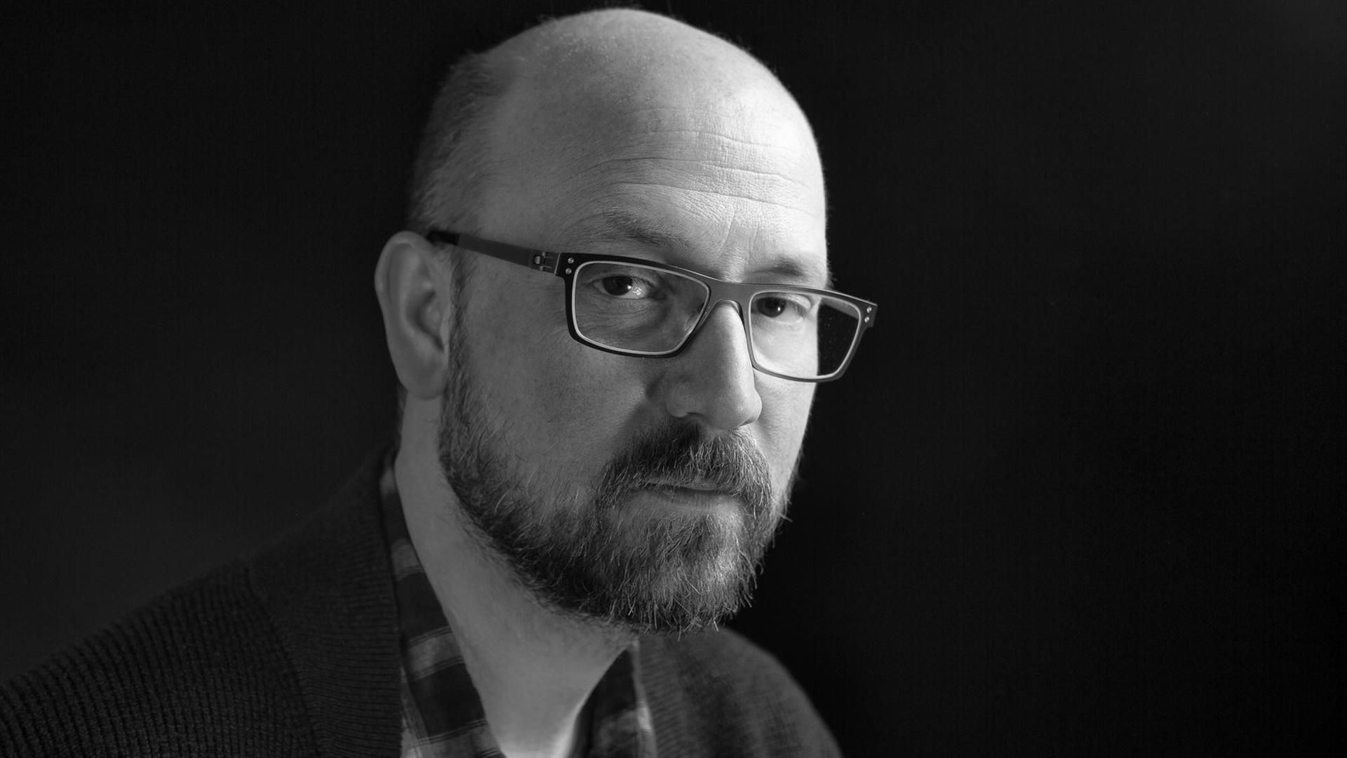 Schwarz-Weiß-Foto von Chip Cheek. Ein Mann mit Glatze, Bart und Brille.