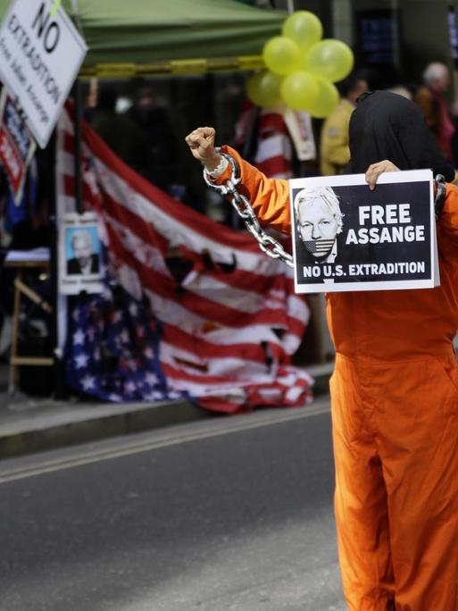 Ein maskierter Demonstrant hat sich als Gefängnisinsasse verkleidet und hält am 1. Oktober 2020 in London ein Schild mit dem Konterfei von julian Assange und der Aufschrift "Free Assange" in der Hand.