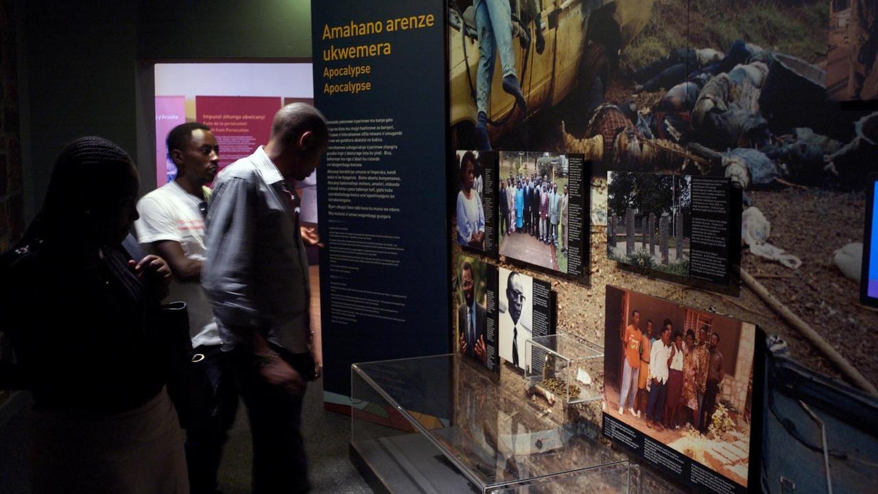 Drei Besucheri*innen schauen sich Ausstellungstafeln im Kigali Genocide Memorial an