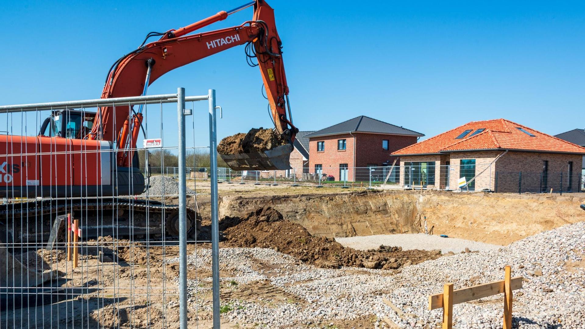 Ein Bagger steht vor einem Neubaugebiet mit Einfamilien- und Mehrfamilienhäusern.