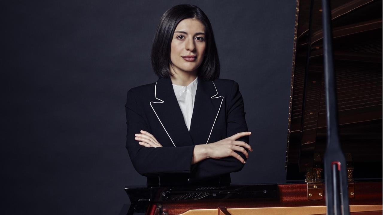 Eine junge Frau mit dunkelbraunen Haaren steht mit verschränkten Armen hinter einem Flügel. Es ist die Pianistin Mariam Batsashvili.