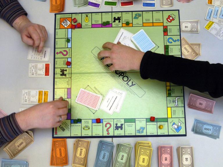 Hände an einem Monopoly-Spielbrett