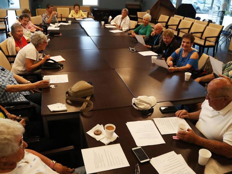 Das Foto zeigt einen jiddischen Debattier-Club in Delray Beach, Florida. Mehrere ältere Damen und Herren sitzen an einem runden Tisch und sprechen miteinander.