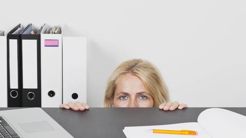 Eien Frau versteckt sich hinter einem Schreibtisch im Büro.