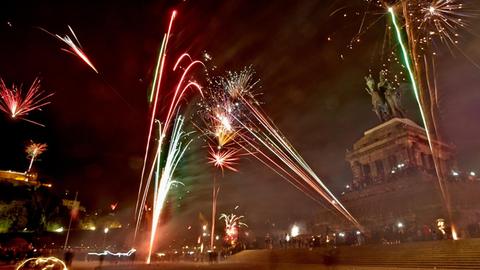 Menschen schießen vor dem Denkmal am Deutschen Eck in der Nacht Raketen in die Luft.