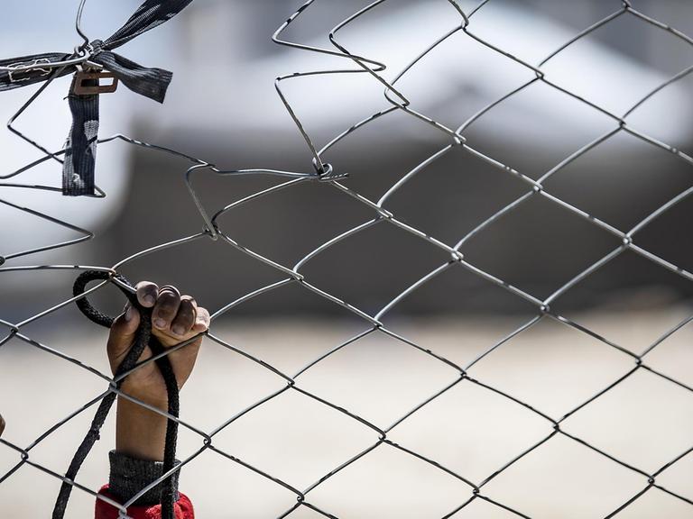 Das Bild zeigt die Hände eines Kindes, das an einem Zaun im Lager im Nordosten Syriens versucht ein Band zu befestigen.
