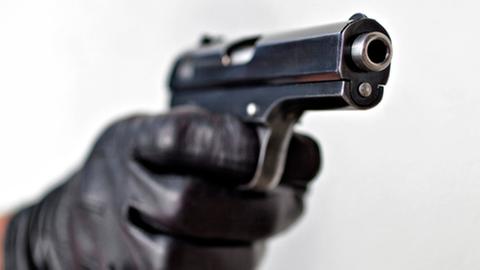 Eine Hand im schwarzen Handschuh hält eine schwarze Pistole.