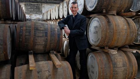 Pfarrer steht vor Whisky-Fässern