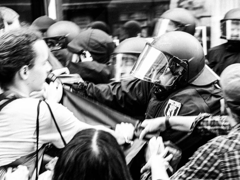 Schwarzweißfoto einer angespannt bis konkret stressigen Situation zwischen Polizei und Hausbesetzern.