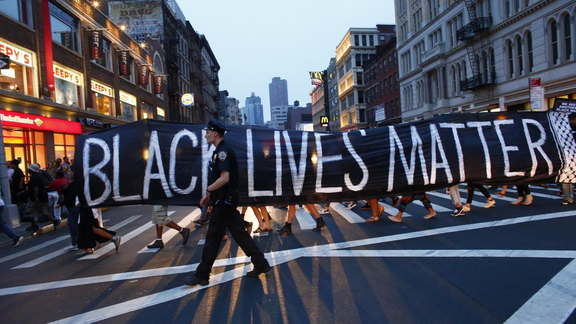 Bei einer Demonstration im Rahmen der "Black-lives-matter"-Bewegung in New York geht ein Polizist vor einem Transparent.