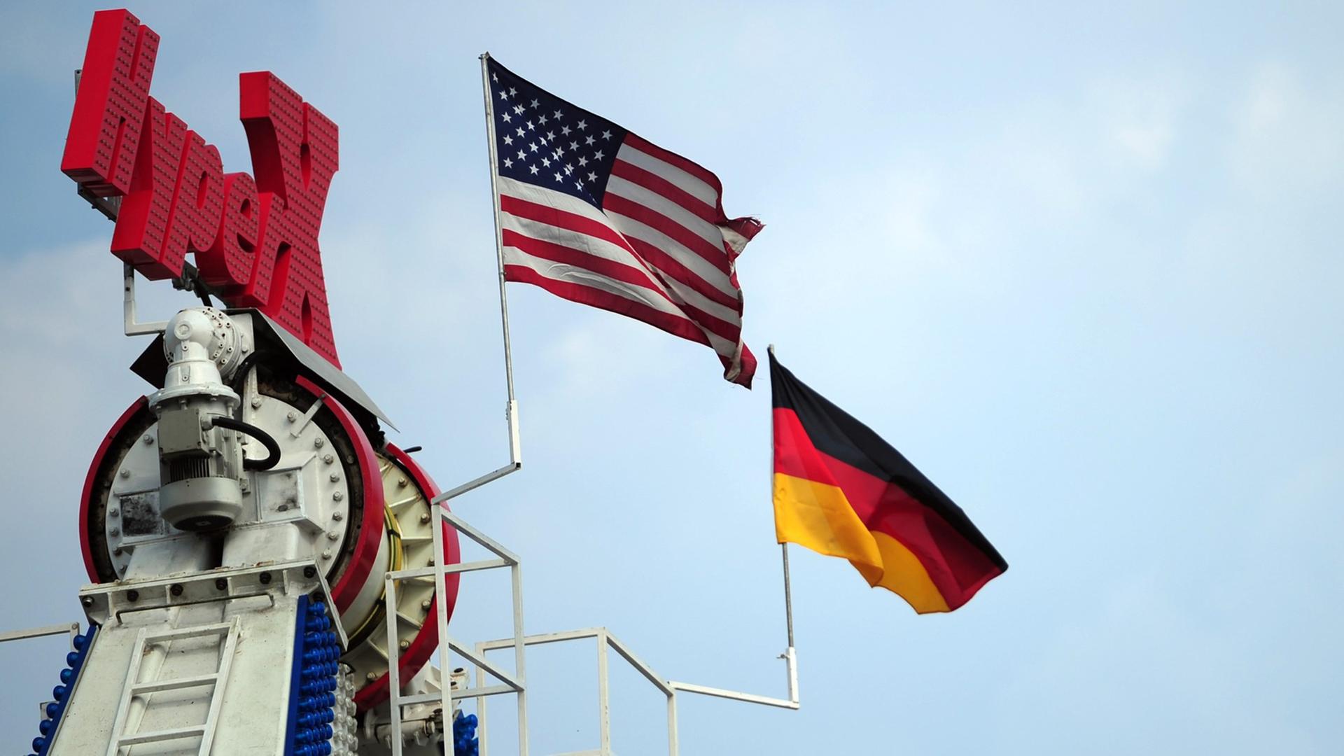 Eine deutsche und eine US-amerikanische Flagge wehen am 26.07.2013 auf dem Gelände des 53. Deutsch-Amerikanischen Volksfestes in Berlin an einem Fahrgeschäft.
