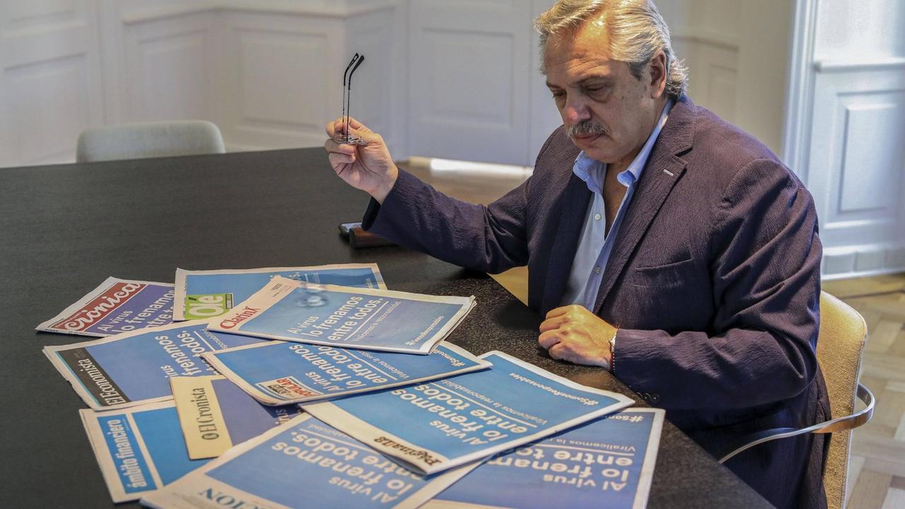 Alberto Fernández sitzt an einem Tisch mit Zeitungen vor sich, die mit Schlagzeilen zum Coronavirus aufmachen.