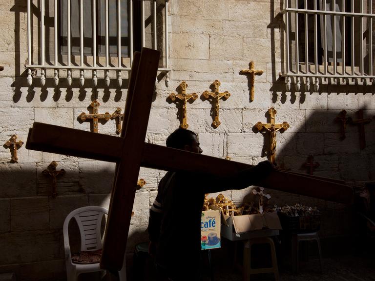 Ein palästinensischer Mann trägt ein Kreuz an den Beginn der Via Dolorosa in Jerusalem zurück.