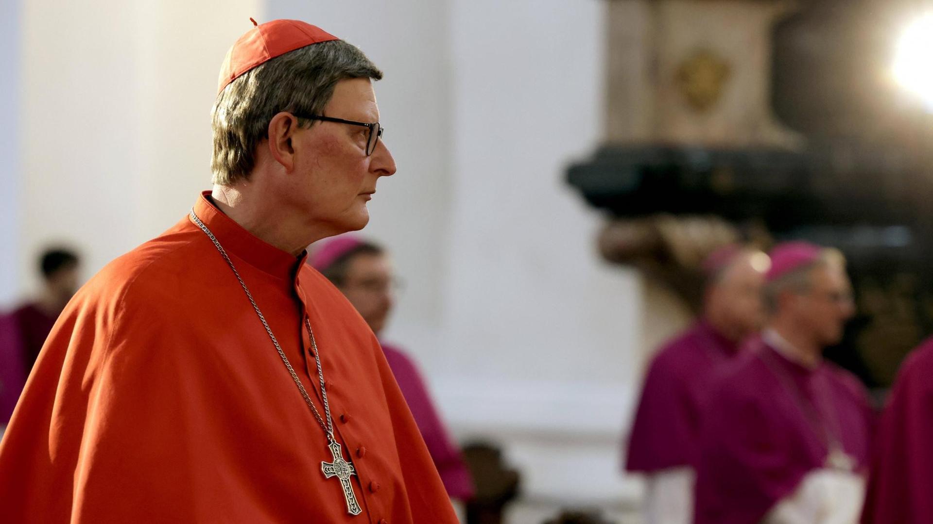 Kardinal Rainer Maria Woelki sitzt in einem roten Gewand in einem Raum und guckt traurig.
