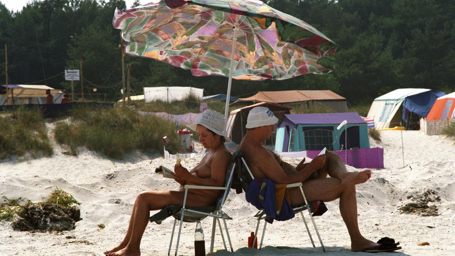 Ein Ehepaar auf einem FKK-Zeltplatz unter einem Sonnenschirm.