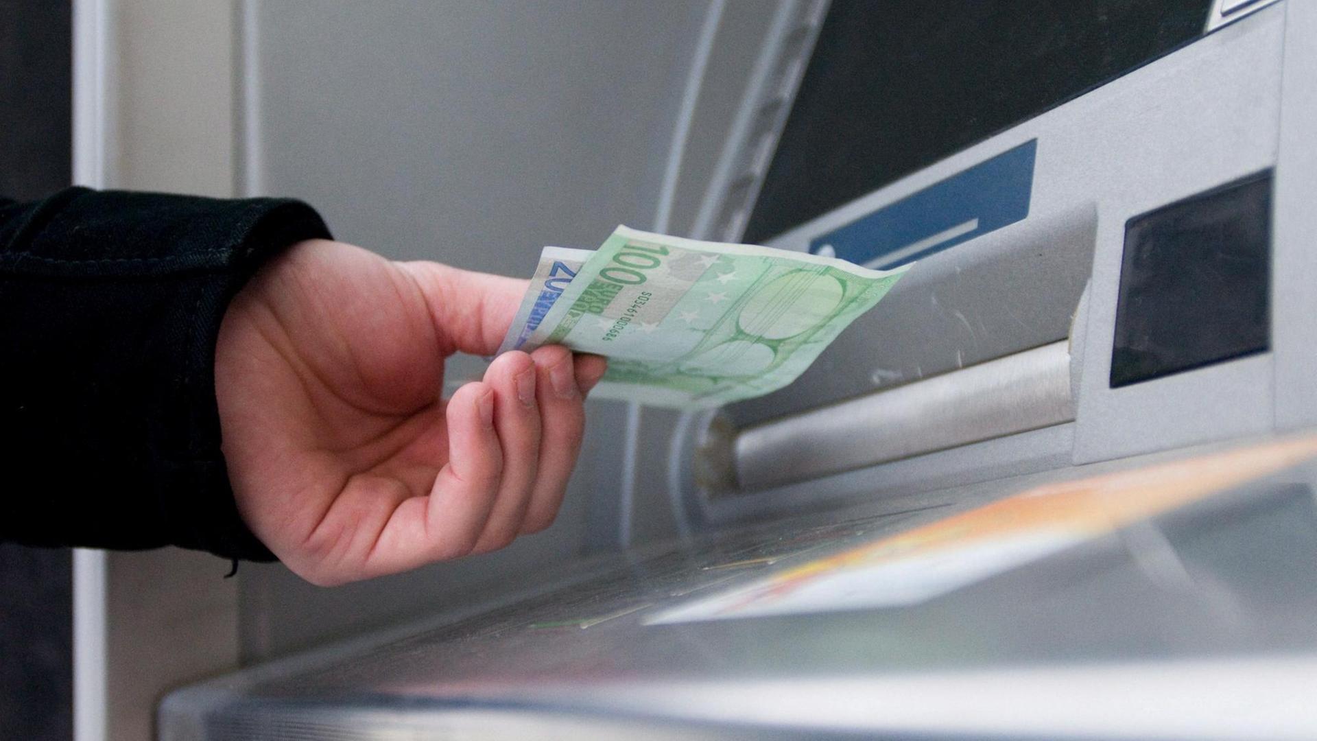 Eine Hand nimmt Geld aus einem Geldautomaten.