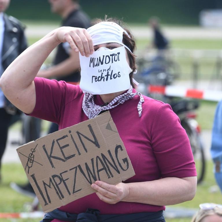 Eine Teilnehmerin einer Demonstrationen gegen die Anti-Corona-Maßnahmen der Politik steht auf der Theresienwiese in München und hält ein Schild mit der Aufschrift "Kein Impfzwang" in der Hand. Auf ihrem Mundschutz steht "Mundtot und rechtlos". 