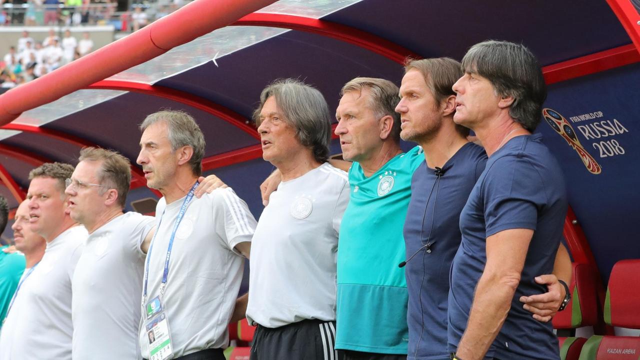 DFB-Bundestrainer Joachim Löw (r.) und Mannschaftsarzt Tim Meyer (2.v.l.) stehen bei der Nationalhymne zusammen vor der Bank. 