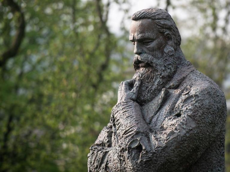 Die Statue Friedrich Engels' in Denkerpose ist ein Geschenk Chinas an die Stadt Wuppertal. Engels guckt nachdenklich zu Boden und streicht sich mit einer Hand den Bart.