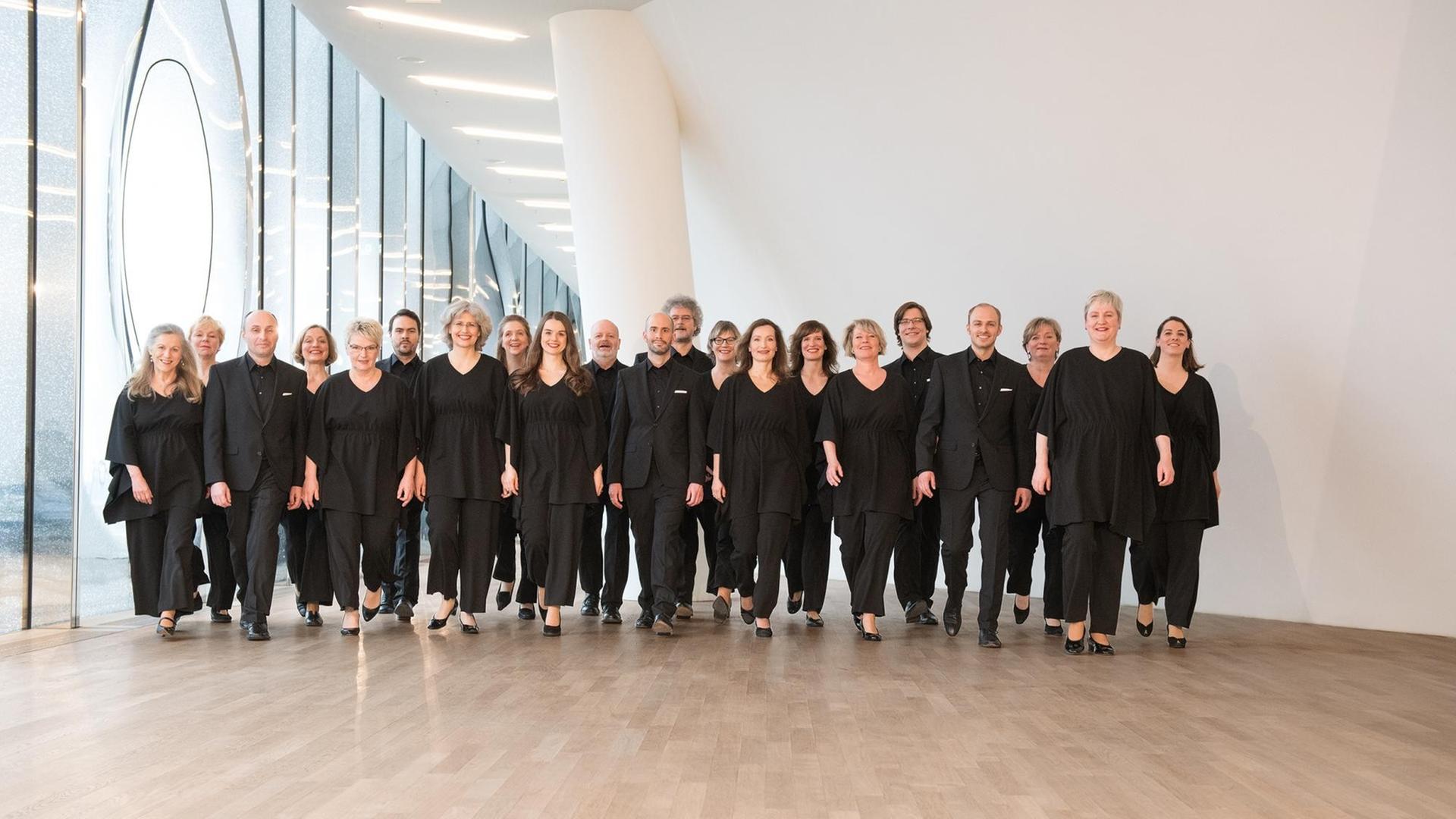 Eine Gruppe von schwarz gekleideten Sängerinnen und Sängern steht halb vor einer Glasfassade, halb vor einer weißen Wand. Im Jahr 2018 posierte der NDR Chor in der Hamburger Elbphilharmonie.