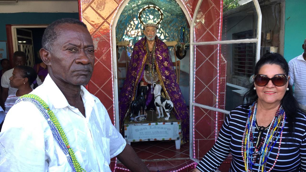 Der Babalao Andres Hernandez steht mit einer Frau vor der Statue des Heiligen Lazarus.