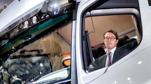 Man sieht Scheuers Gesicht klein durch das Seitenfenster des Transporters.