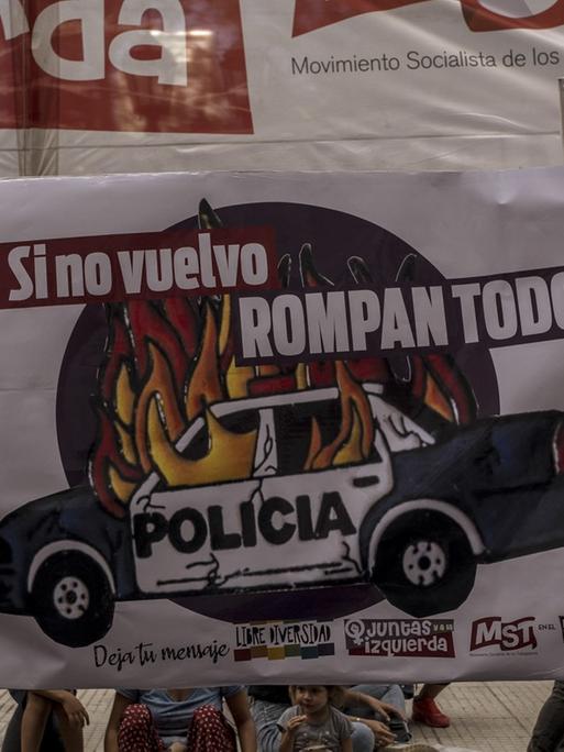 Auf einer Demonstration tragen zwei Frauen mit Mundschutz ein Banner mit einem brennenden Polizeiauto.