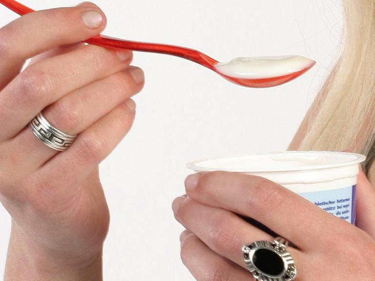 Eine Hand hält einen roten Löffel mit Joghurt.