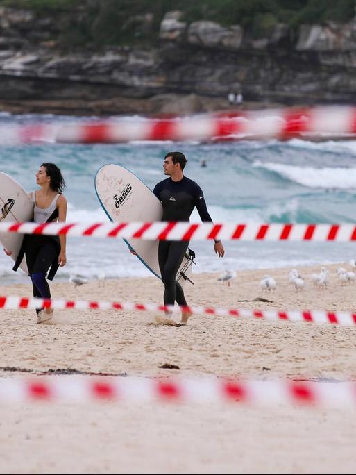 Eine wenige Surfer am Bondi Beach in Sydney, Australien, im Vordergrund ist Absperrband zu sehen, aufgenommen im April 2020