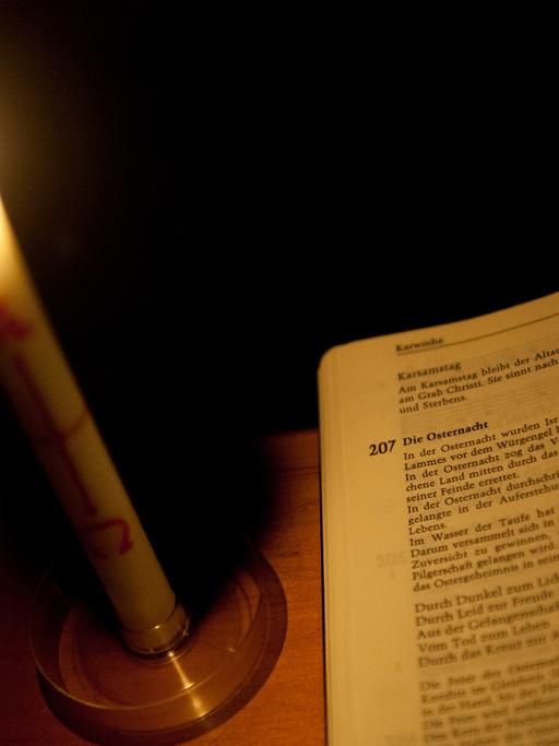 Eine Kerze steht in der Ostermesse in der katholischen Kirche St. Michael in Kassel (Hessen) neben einem Gesangbuch.