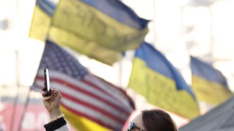 Eine ukrainische Frau nimmt ein Foto in Kiev auf. Im Hintergrund ukrainische und US-amerikanische Flaggen.