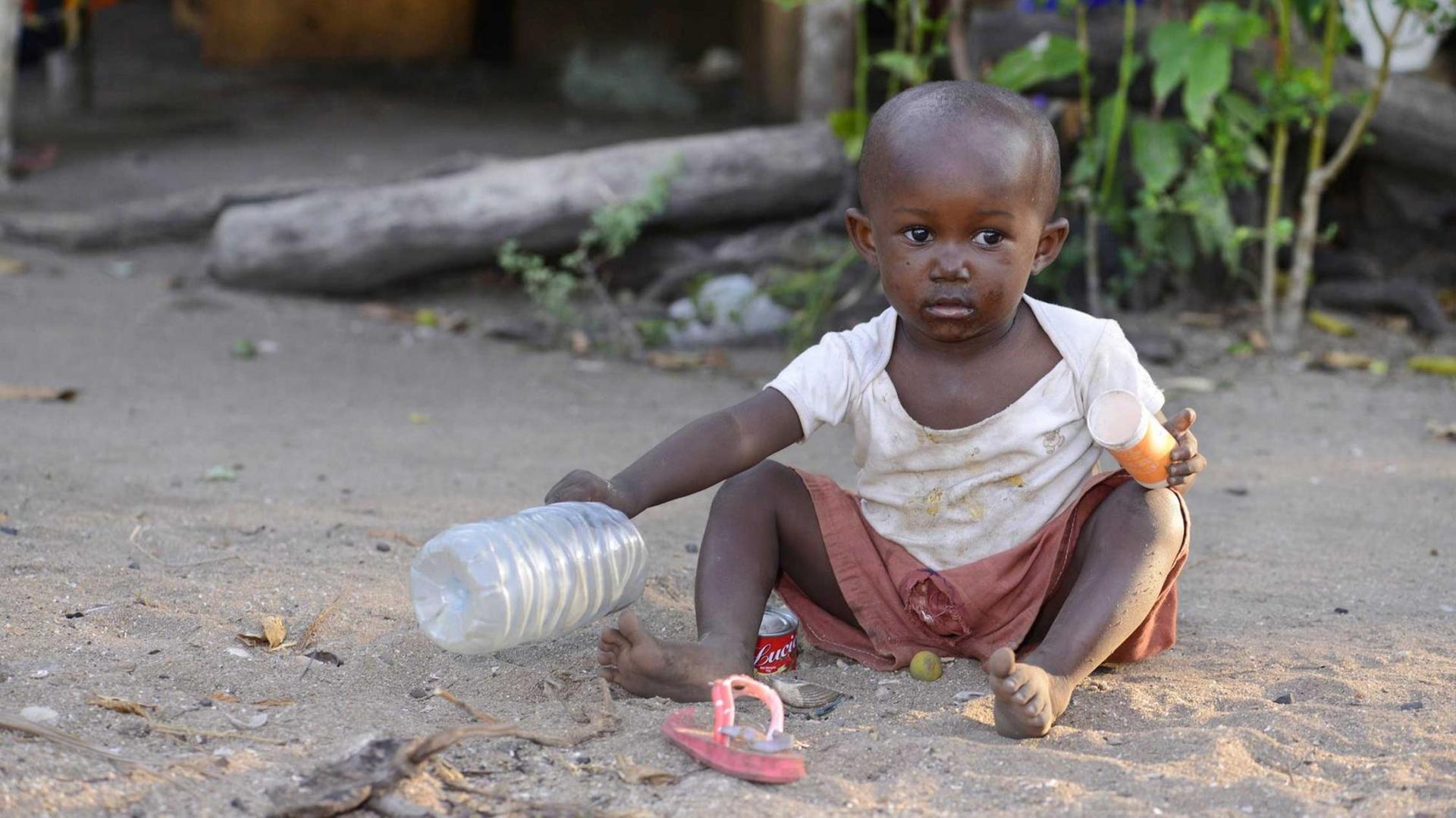 Kleiner Junge mit einer leeren Wasserflasche sitzt auf dem Boden