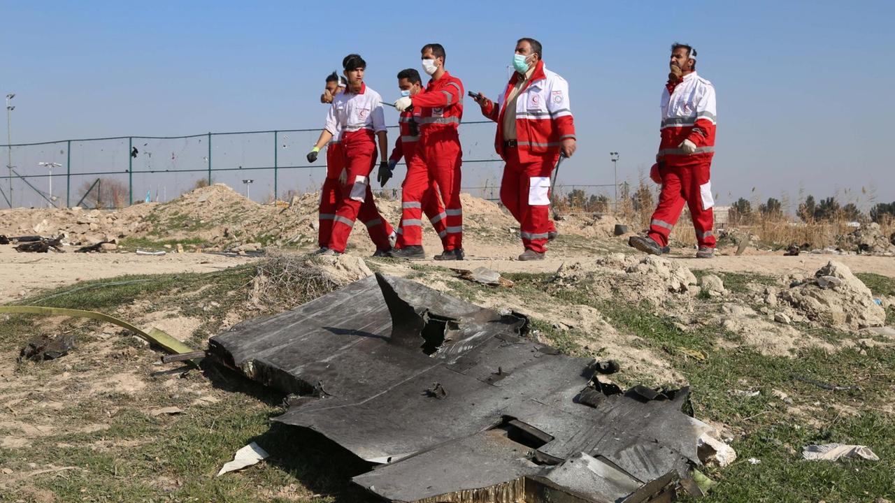 Einsatzkräfte in roten Overalls am 8. Januar 2020 an der Unglücksstelle, an der ein ukrainische Flugzeug bei Teheran abgestürzt ist, im Vordergund des Bildes liegen Trümmer.