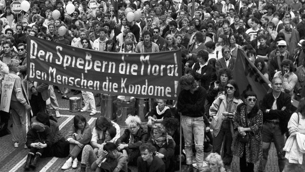 Eine Menschenmenge demonstriert unter em Motto "Gegen Aids – für Vernunft" in München. In der Bildmitte ist ein Transparent mit der Aufschrift "Den Spießern die Moral, Den Menschen die Kondome!" zu sehen.