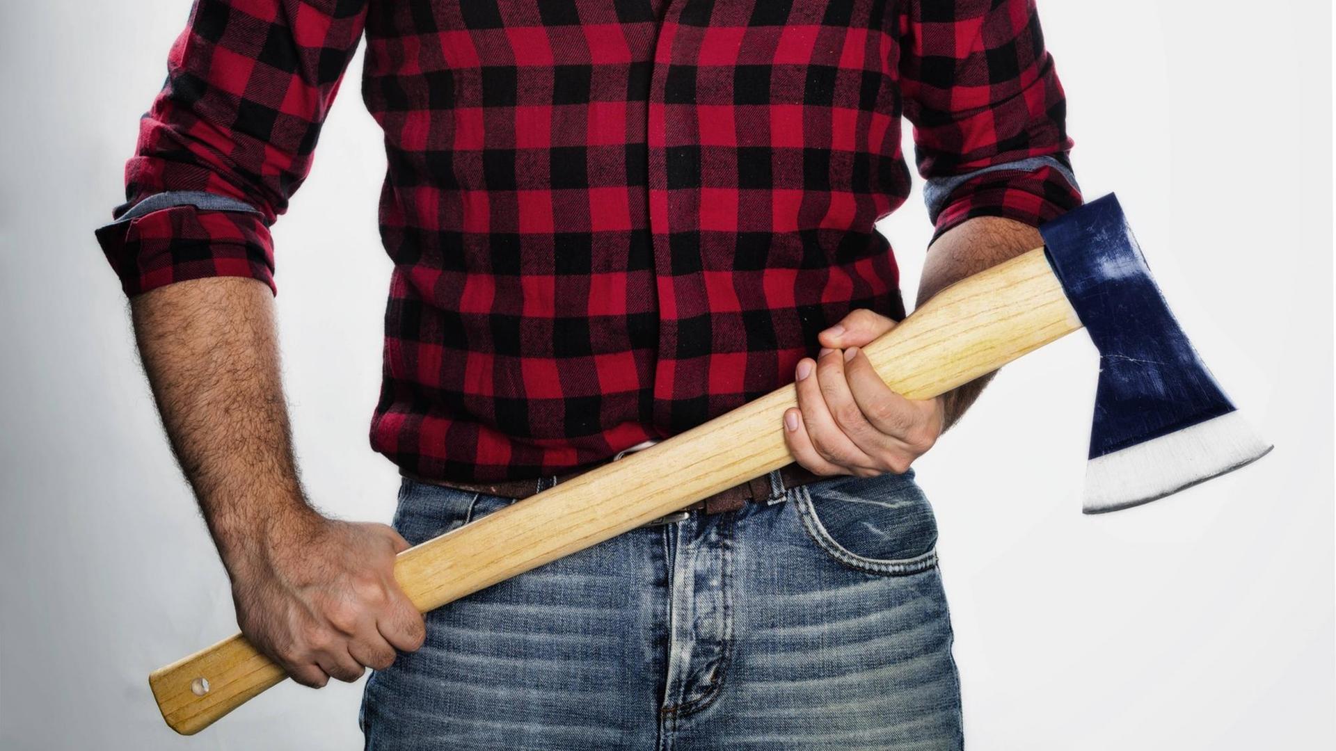 Ein Mann im karierten Hemd trägt eine Holzfäller-Axt.