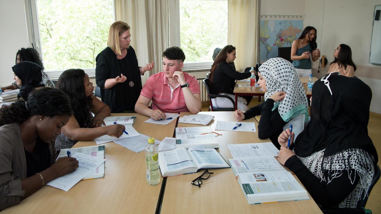 Unterrichtssequenz in der Berliner Berufsfachschule Paulo Freire: Schülerinnen und Schüler sitzen an Tischen und eine Lehrerin steht und spricht. 
