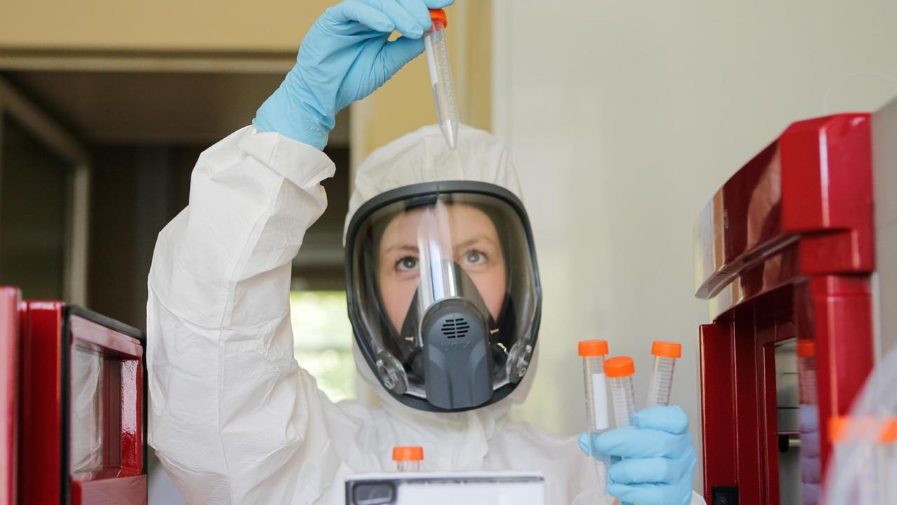 Das Foto zeigt eine Forscherin in einem Labor, im Schutzausrüstung und mit Reagenzgläsern in den Händen.