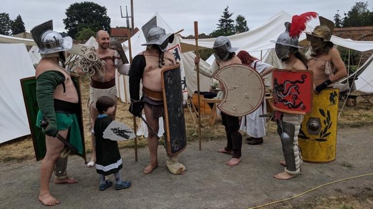 Sechs Personen sehen mit Schildern, Schwert, Helmen und Beinschienen aus wie Gladiatoren.