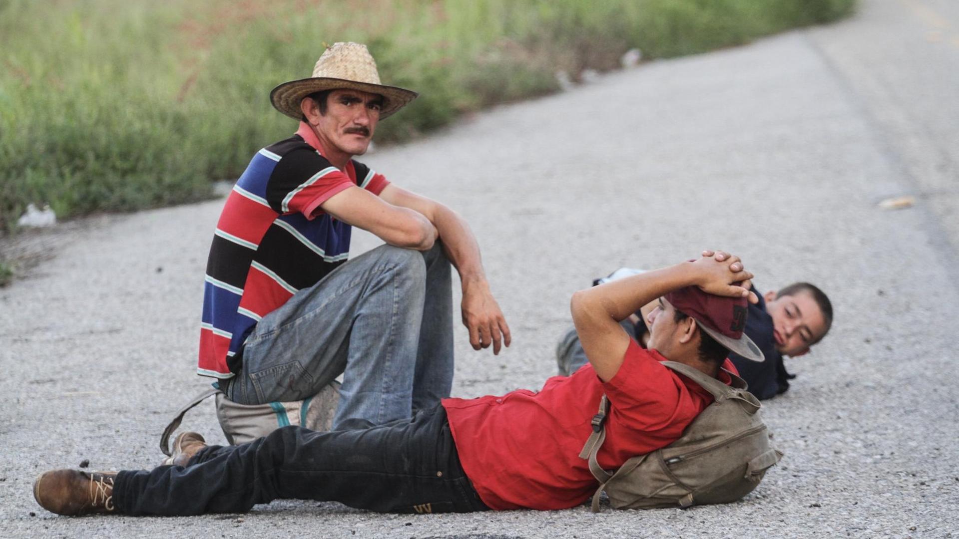 Drei Migranten aus Mittelamerika sitzen auf ihrem Weg in Richtung USA auf der Straße. Foto: Isaac Monroy/dpa | Verwendung weltweit