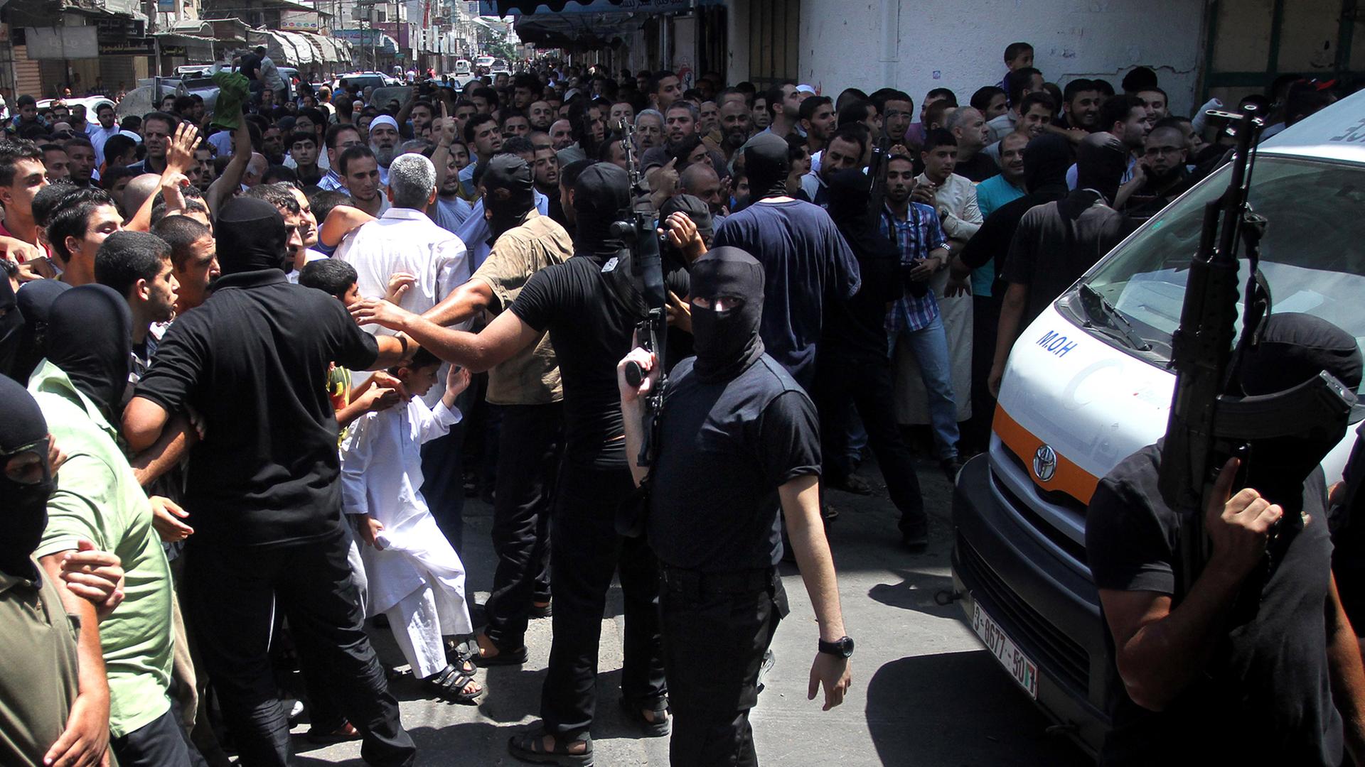 Maskierte militante Palästinenser halten eine Menschenmenge vor einer Moschee in Gaza-Stadt in Schach.
