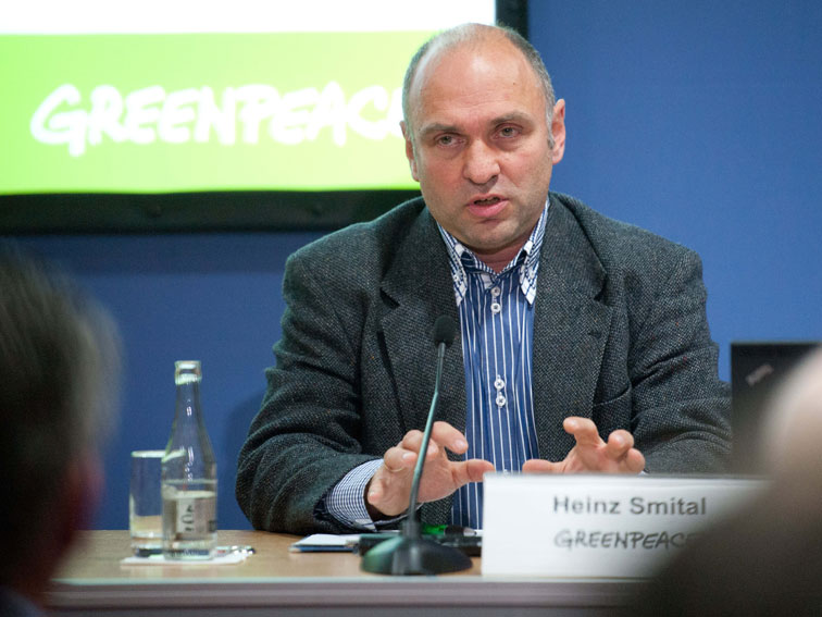 Heinz Smital sitzt vor einem Mikrofon, im Hintergrund ein Monitor mit Greenpeace-Aufschrift. Im Vordergrund sind Zuhörer zu erkennen.